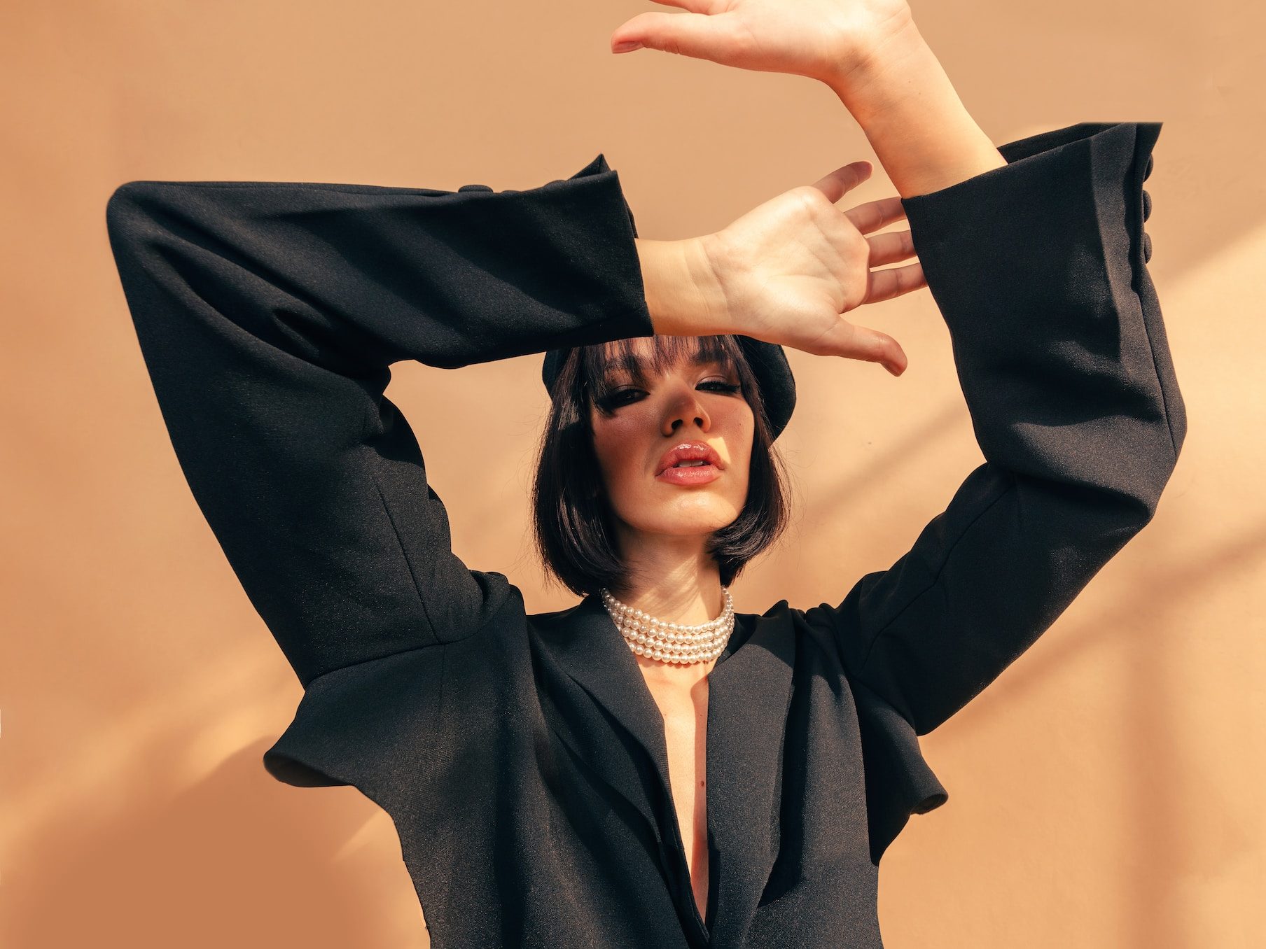 fashion photo about woman wear a black loose jacket and a 4 layer pearl tight necklace, raising her arms wide up above like covering sunlight to her face
